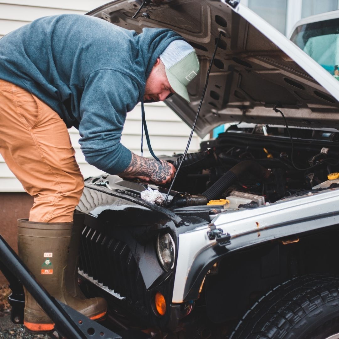 man standing over top of jeep working on engine
